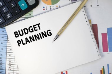 Bütçe planlaması, sayılardan oluşan sütunlar ve siyah hesap makinesi içeren finansal bir belgenin üzerine yazılmış bir defterde bulunur. İş ve mali konsept