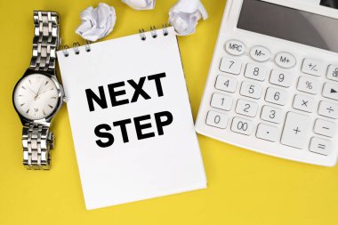 Yazı, beyaz bir hesap makinesinin yanında sarı bir arkaplanda duran bir deftere ve buruşuk kağıt yapraklı bir kol saatine yazılmıştır..