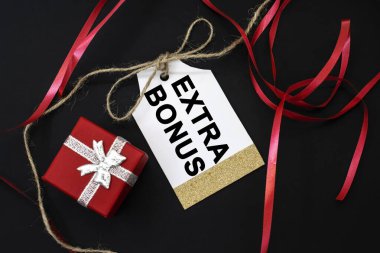 Siyah arka planda yer alan satış etiketine ek bir bonus daha yazılır. Kırmızı bir kurdele ve hediye kutusu. Müşteri çekmek için indirim kavramı