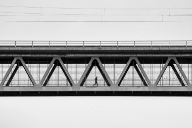 Bir adam demir bir köprünün metal mekanizmasında koşuyor.