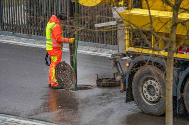 Sokakta kanalizasyon temizleme aracının arkasında çalışan tanınmayan bir adamla rögar kapağında çalışıyorum..