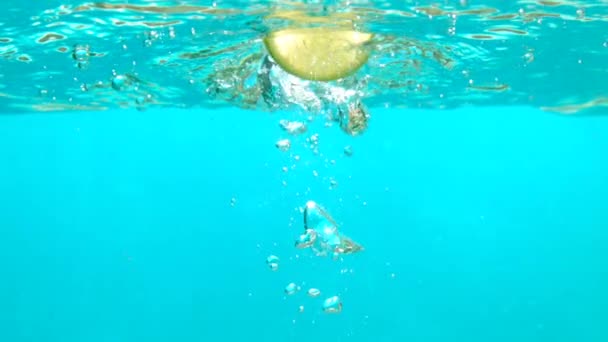 Kék vízben a lassú víz alatti szemcsésedik asztali buborékok esik szelet citrommal — Stock videók