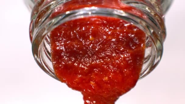 Ketchup lub Sos czerwony jest wylewanie z makro butelki szklane w zwolnionym tempie białe tło blatem — Wideo stockowe