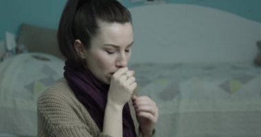 Kadın öksürüyor. Atkıya sarılıp termometreyle sıcaklığı kontrol ediyor.