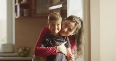 Anne ve Çocuk Portresi Gülümseyen ve Kameraya Bakan Güneşli bir günde Mutfakta Duran