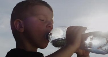 Küçük çocuk arka planda Arkaplan Güneşi ve Mavi Gök ile Dışarıdaki Şişeden Su İçiyor Yakın plan Çekimi