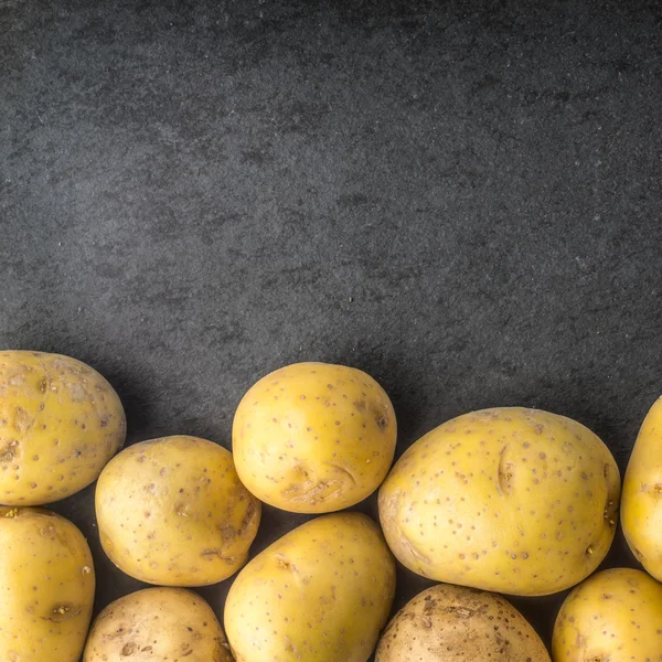 Rå potatis på svart sten bordet kvadrat — Stockfoto