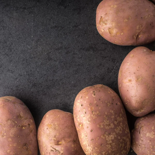 Rå potatis till höger om den svarta stenen tabell square — Stockfoto