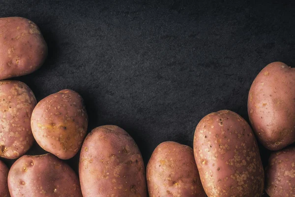 Batatas cruas na mesa de pedra preta — Fotografia de Stock