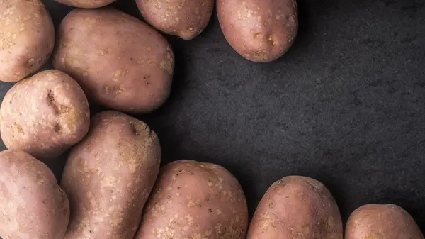 Batatas cruas na mesa de pedra escura horizontal — Fotografia de Stock