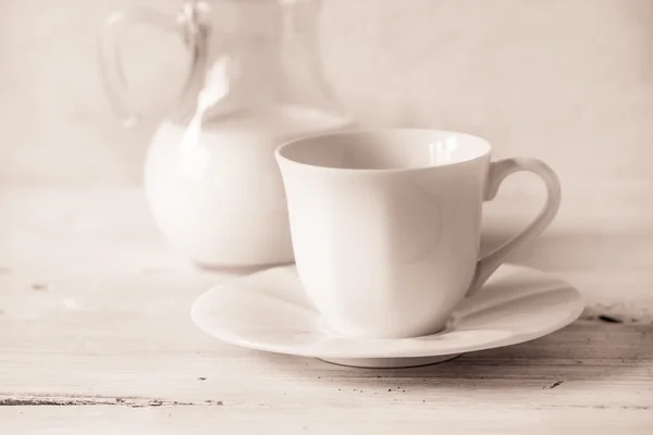 Xícara de café com jarro desfocado de leite na mesa branca — Fotografia de Stock