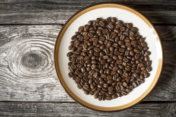 Kaffeebohnen auf dem Teller auf der Holztischplatte — Stockfoto