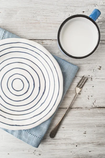 Керамическая плита с вилкой и чашкой молока на деревянном столе вертикально — стоковое фото