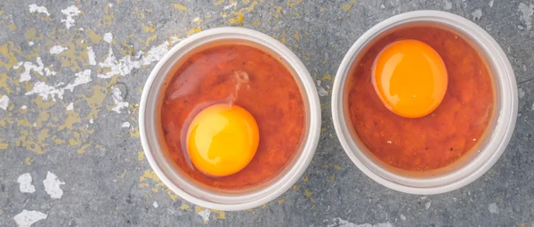Råa ägg med tomater i ramekins på stenen bord widescreen — Stockfoto