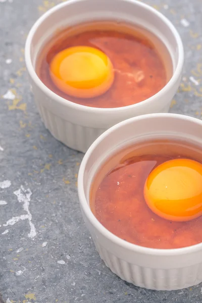 Raw eggs with tomatoes in the ramekins on the stone table vertical — Stock Photo, Image