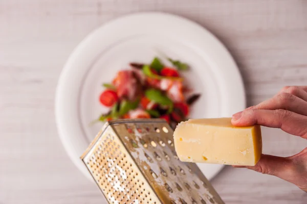 Mulher moagem queijo ralado em uma salada de tomate e presunto — Fotografia de Stock