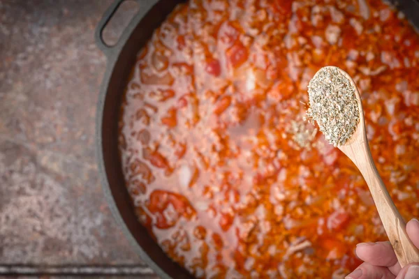 Łyżkę ziół na niewyraźne garnka gulasz mięso i pomidory — Zdjęcie stockowe