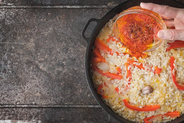 Добавление шафрана в кастрюлю с рисом и перцем сверху — стоковое фото