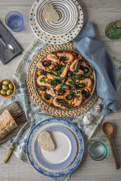 Paella on the metal plate on the beautiful napkin with tableware and bread vertical — Stock Photo, Image