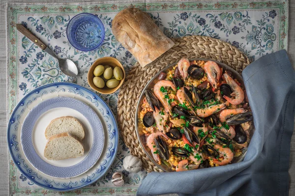 Paella on the metal plate on the beautiful napkin with tableware and bread top view — Stock Photo, Image