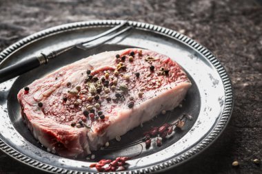 Ribeye Steak on a tin plate, fork and barberry berries on a ston