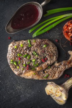 Grilled ribeye steak, sauce, garlic and tomatoes on a wooden boa