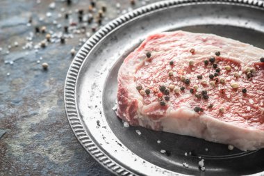 Piece of ribeye steak and peppercorn and salt on a plate of tin