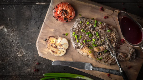 Filete de Ribeye a la parrilla, ajo y tomates en una tabla de madera — Foto de Stock