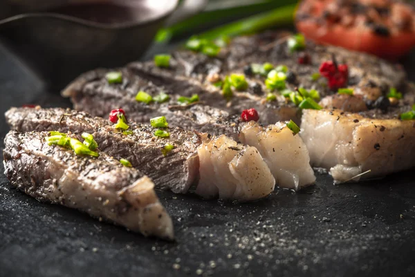 Strips of grilled ribeye steak, gravy boat, onions, and tomatoes — Stock fotografie