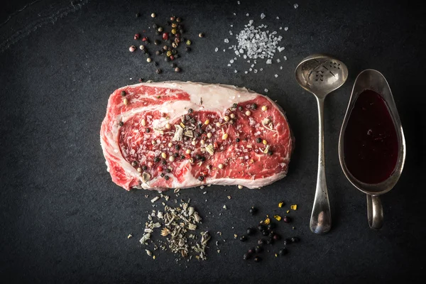 Marble ribeye steak, juniper, spoon, gravy boat on a blue-black — Stock fotografie