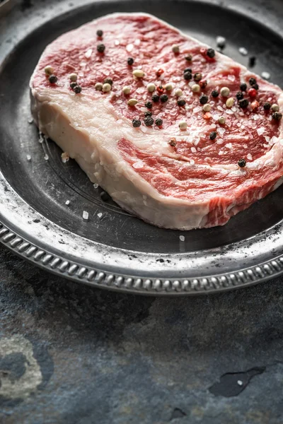 Trozo de bistec de ribeye y pimienta y sal en un plato de estaño —  Fotos de Stock