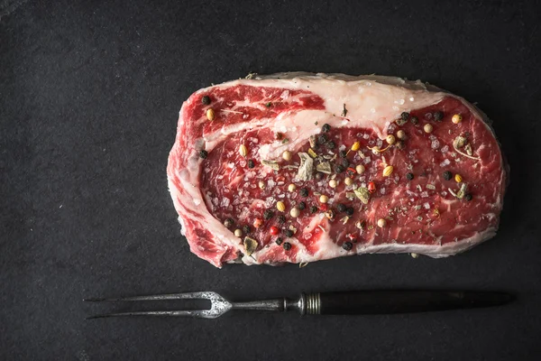 Filete de ribeye de mármol, pimienta, salvia, tenedor en piedra negra — Foto de Stock