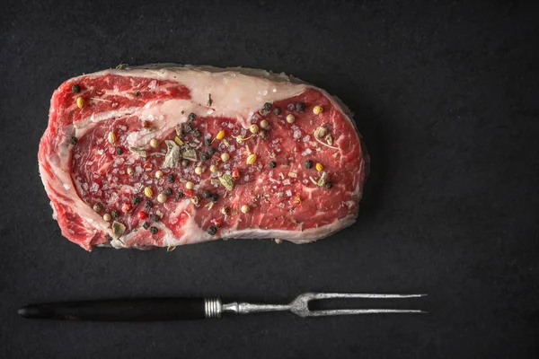 Ribeye steak, svartpeppar, salvia, gaffel på svart sten — Stockfoto