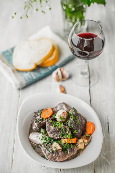 Beef bourguignon in a white ceramic plate with a glass of wine — Stock Photo, Image