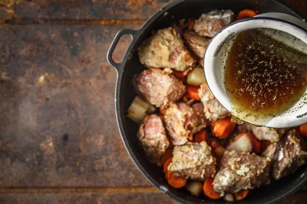 Het toevoegen van Bouillon in de pan met vlees- en plantaardige bovenaanzicht — Stockfoto