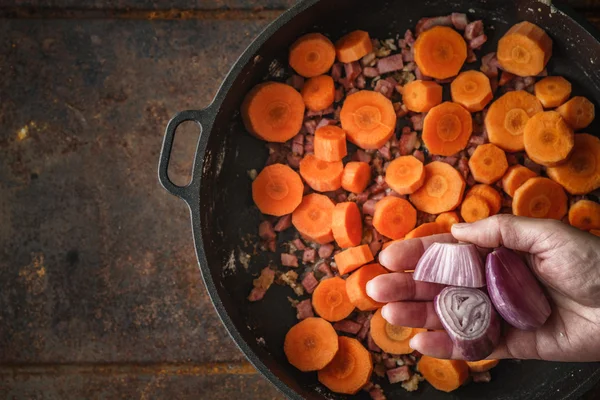 Att lägga schalottenlök i pannan med bacon och morötter ovanifrån — Stockfoto