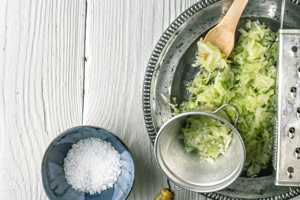 Grated cucumber with strainer and salt on the white table  top view — Stock Photo, Image