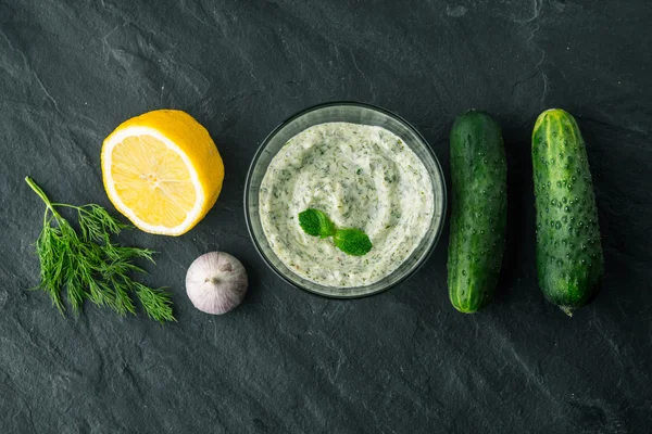 Tzatziki på det mörka stenbord med ingredienser ovanifrån — Stockfoto