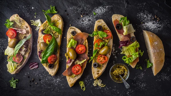 Slices of ciabatta with olives , tomatoes and basil on the black stone table wide screen — Stock Photo, Image