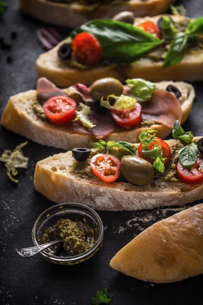 Rebanadas de ciabatta con aceitunas, tomates y albahaca en la mesa de piedra negra vertical — Foto de Stock