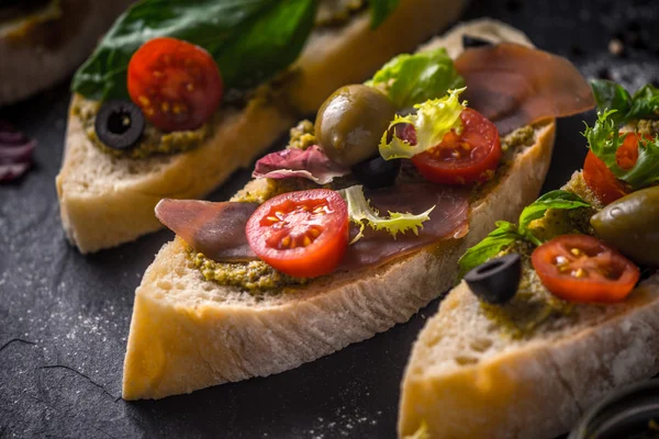 Slices of ciabatta with olives , tomatoes and basil on the black stone table horizontal — Stock Photo, Image