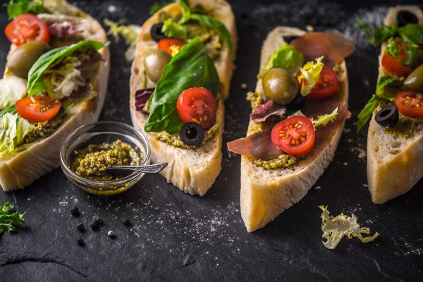 Rebanadas de ciabatta con aceitunas, tomates y albahaca en la mesa de piedra negra — Foto de Stock