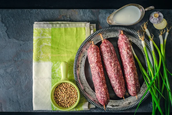 Raw kebabs with green onions and garlic on the stone table top view — Stock Photo, Image