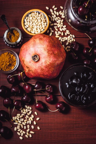 Stillleben mit Granatapfel, Kirsche und Gewürzen auf dem roten Holztisch. Konzept der orientalischen Früchte vertikal — Stockfoto