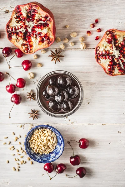 Stillleben mit Granatapfel, Kirsche und Gewürzen auf dem weißen Holztisch. Konzept der orientalischen Früchte — Stockfoto