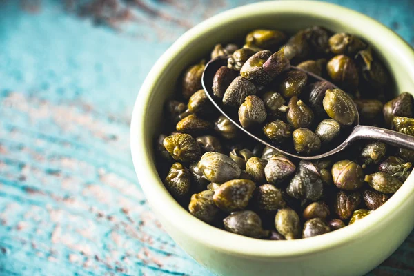 Capers in the bowl on the light blue background — Stock Photo, Image