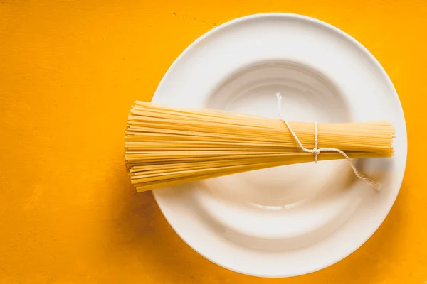 黄色の背景の上面の白いプレートの生スパゲッティ — ストック写真