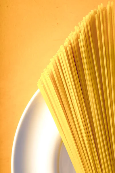 Espaguete cru na placa branca no fundo amarelo vertical — Fotografia de Stock