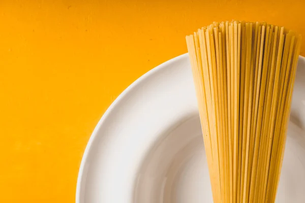 Raw spaghetti  on the white plate on the yellow background — Stock Photo, Image