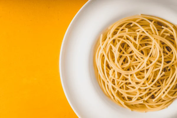 Spagetti på den vita plattan på gul bakgrund ovanifrån — Stockfoto